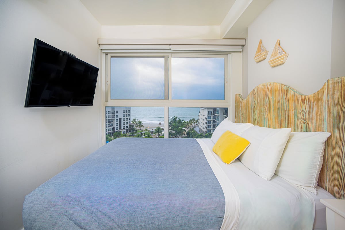 Une chambre d’hôtel dotée d’un grand lit, d’un téléviseur à écran plat fixé au mur et offrant une vue sur l’océan par une grande fenêtre.