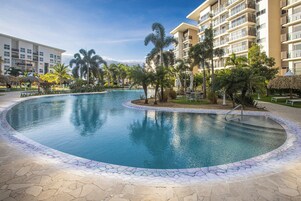 Una piscina con borde de piedra, rodeada de palmeras y sillas de descanso.