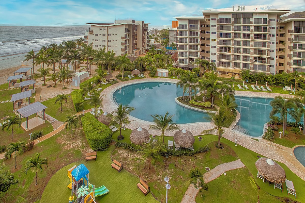 Un complexe hôtelier doté d’une grande piscine, de palmiers et offrant une vue sur la plage.