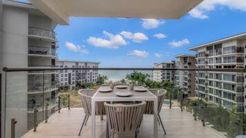 A balcony with a table and chairs, overlooking a beach and other buildings.