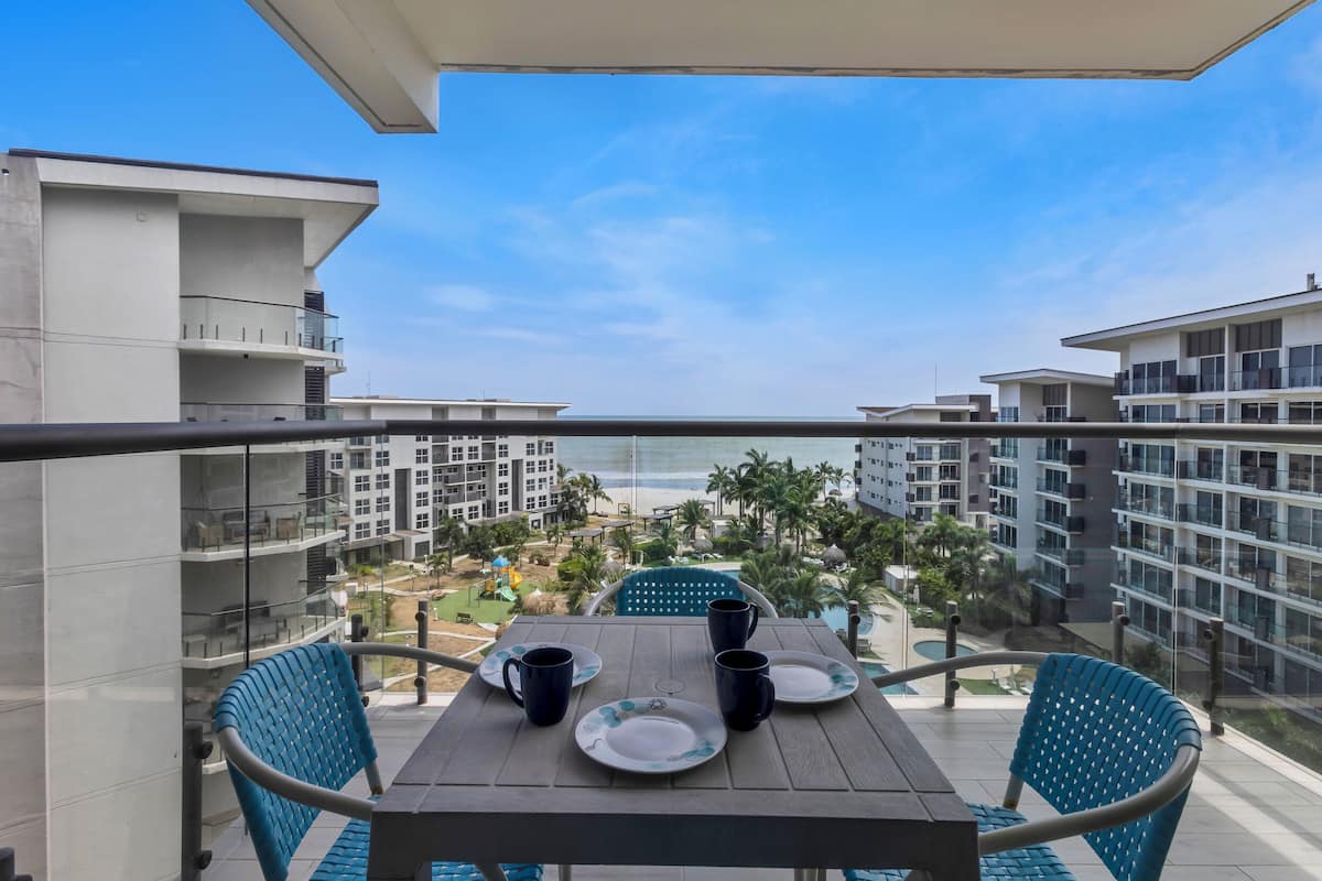 Un balcon avec une table dressée pour deux personnes, donnant sur une piscine et des immeubles.