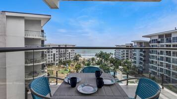 A balcony with a table set for two, overlooking a pool and buildings.