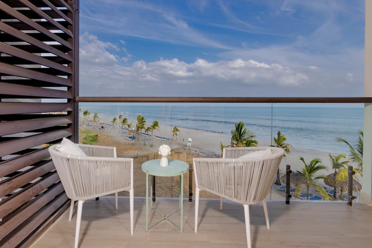 Un balcon agrémenté de meubles en osier, d’une petite table et offrant une vue sur la plage et l’océan.
