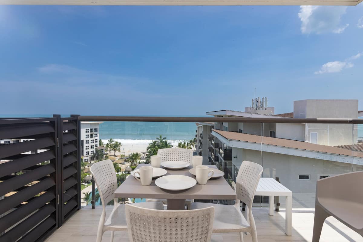 Un balcon avec une table et des chaises, donnant sur une plage et l’océan.