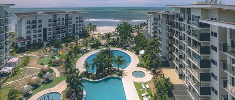 A resort with a large pool, palm trees, and a view of the ocean.