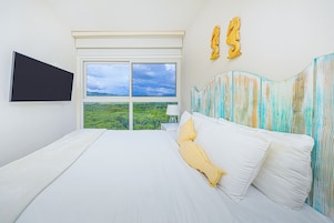 Un dormitorio con una cama grande, un televisor montado en la pared y vistas a zonas verdes por la ventana.
