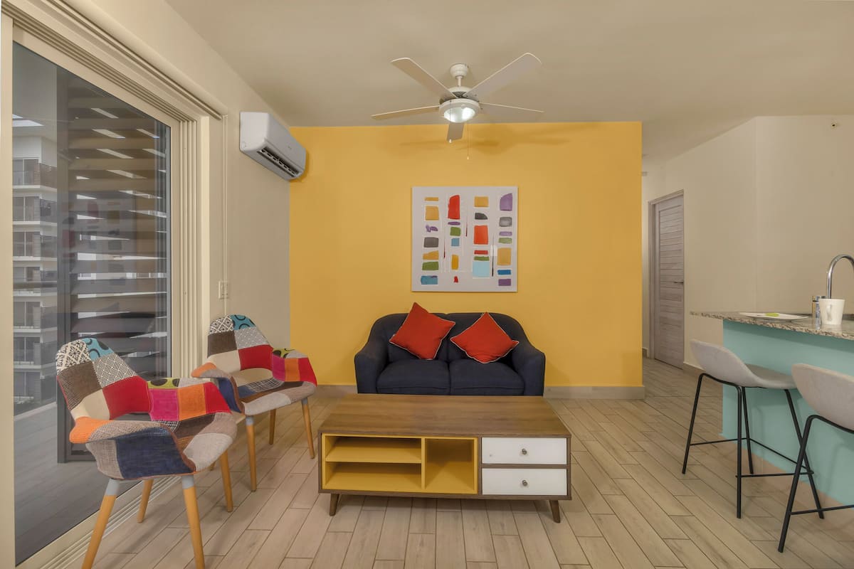 Un salon comprenant un canapé, des fauteuils, une table basse, un ventilateur de plafond et un climatiseur fixé au mur.