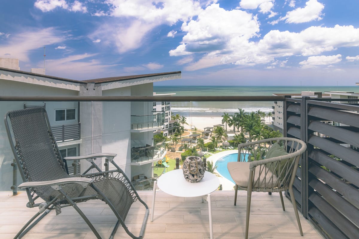 Un balcon avec vue sur la plage, une piscine et un espace détente avec des chaises et une table.