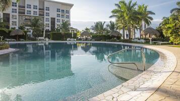 A pool area with a stone border, lounge chairs, and palm trees.