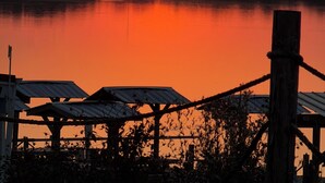Een zonsondergang boven een rustig meer, met een houten steiger en een metalen constructie op de voorgrond.