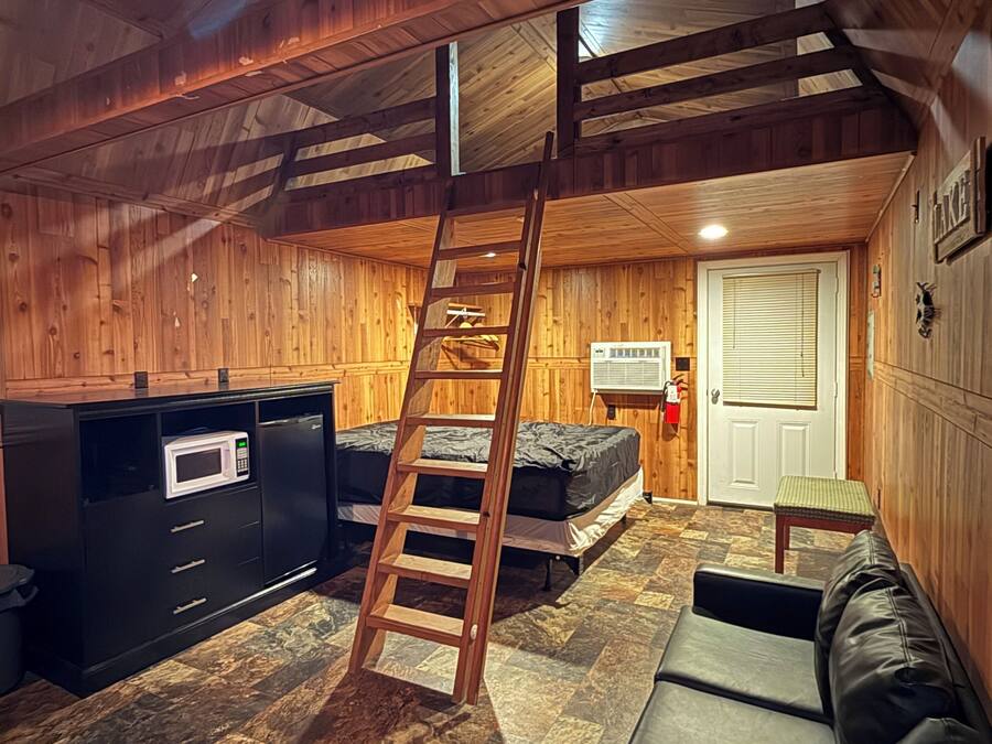Un chalet confortable doté d’un lit en mezzanine, d’une échelle menant à l’espace de couchage supérieur, d’une kitchenette et d’une cheminée.