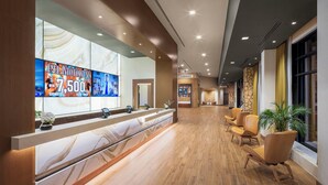 A hotel reception area with a marble counter, multiple screens, and a seating area with chairs. - Golden Mesa Hotel (Guymon)