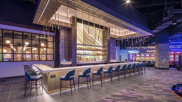 A bar area with a long counter, multiple bar stools, and a cash register. - Golden Mesa Hotel (Guymon)