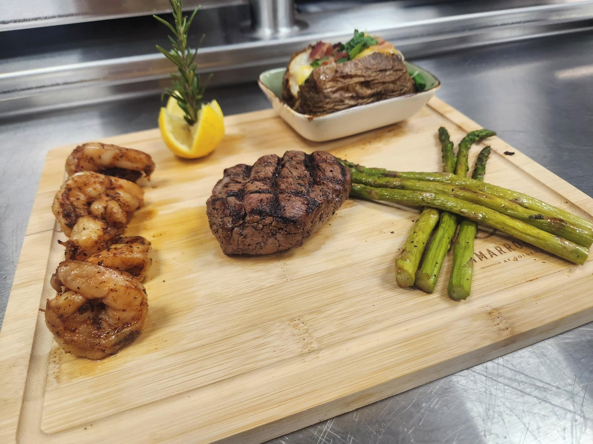 Una tabla de madera con camarones a la parrilla, filete y espárragos.