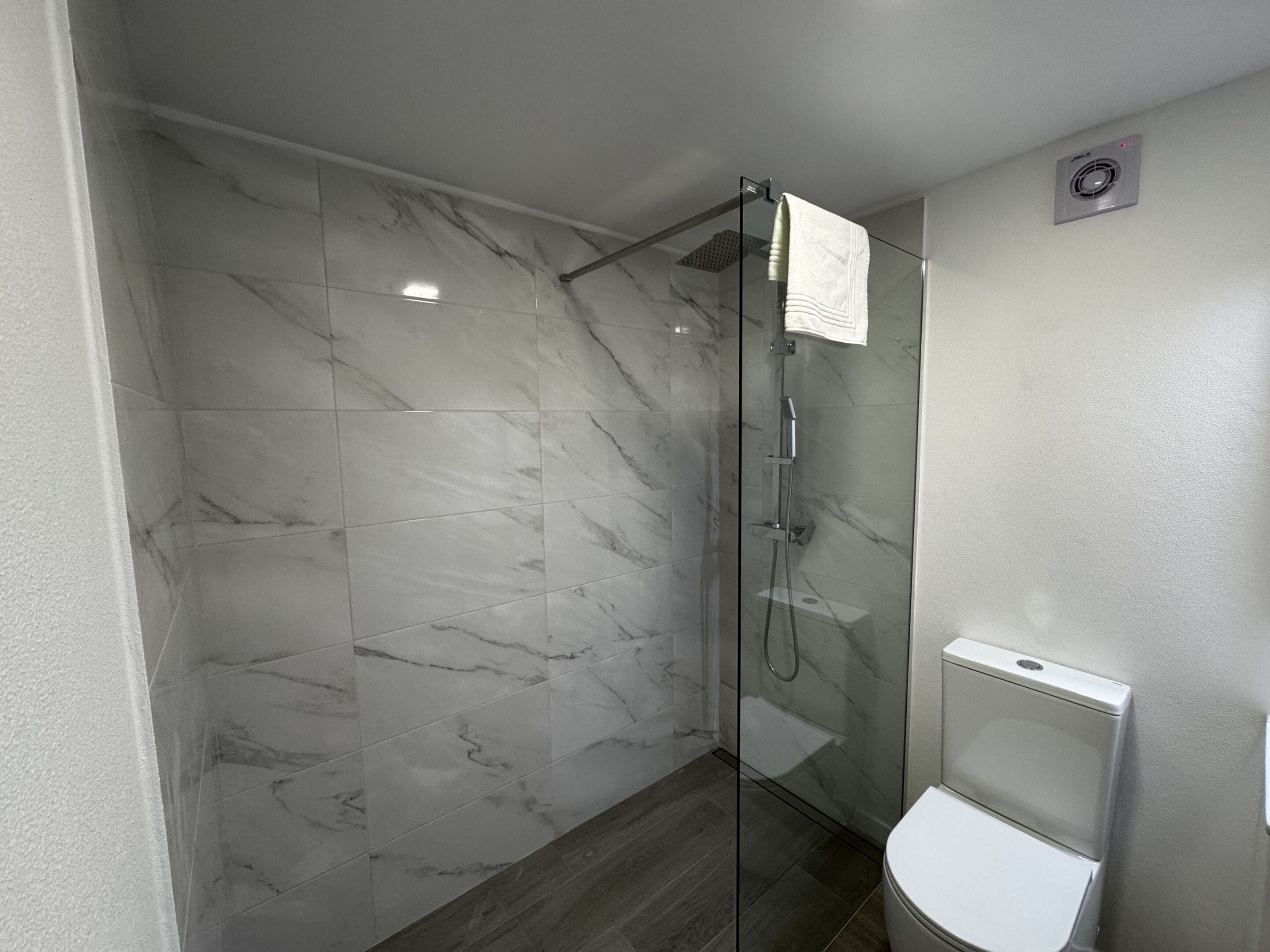 Ein modernes Badezimmer mit einer gläsernen Duschkabine, Marmorfliesen und einer weißen Toilette.