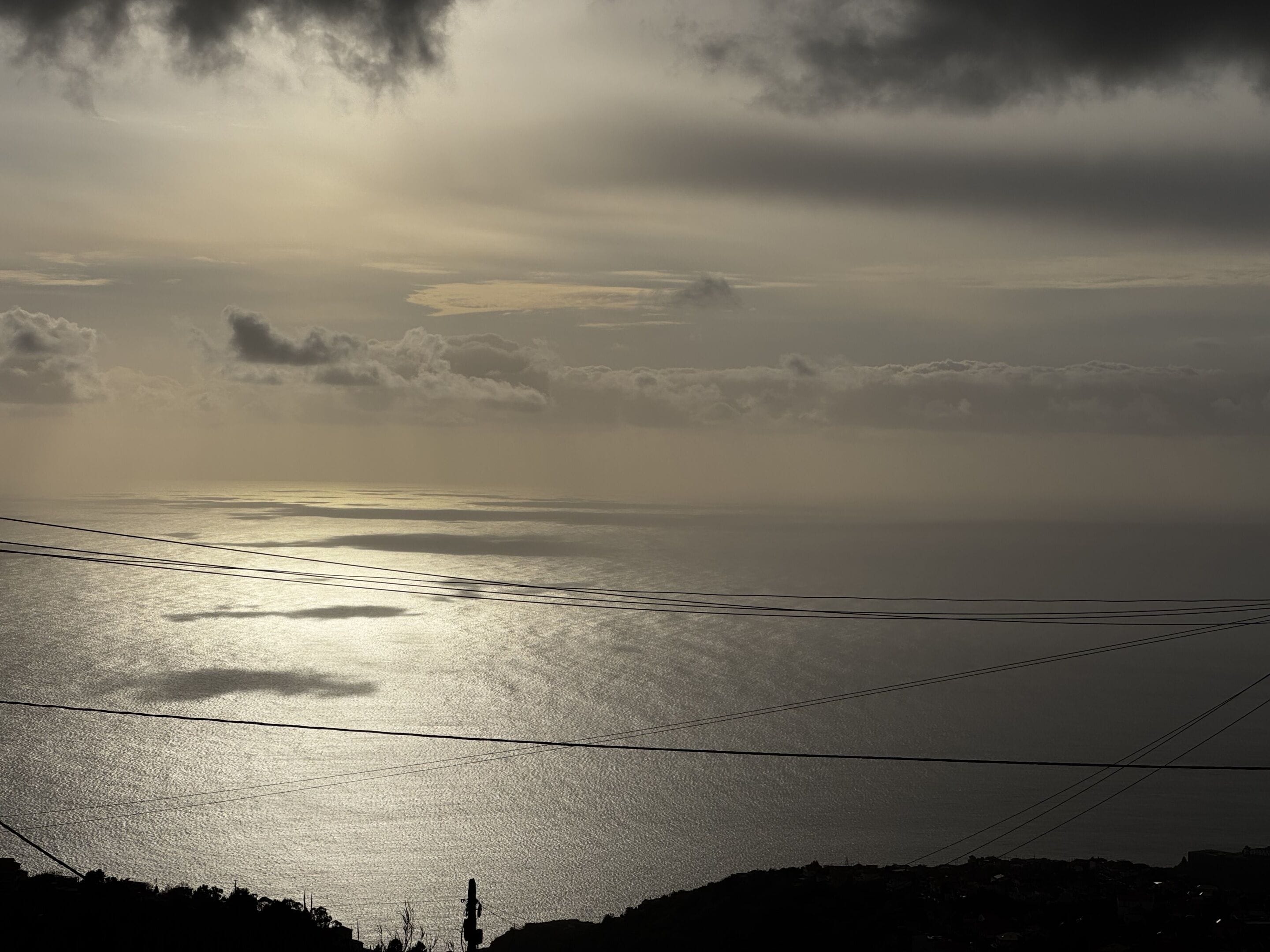 Un paysage côtier avec vue sur la mer et des lignes électriques qui traversent l’étendue d’eau.