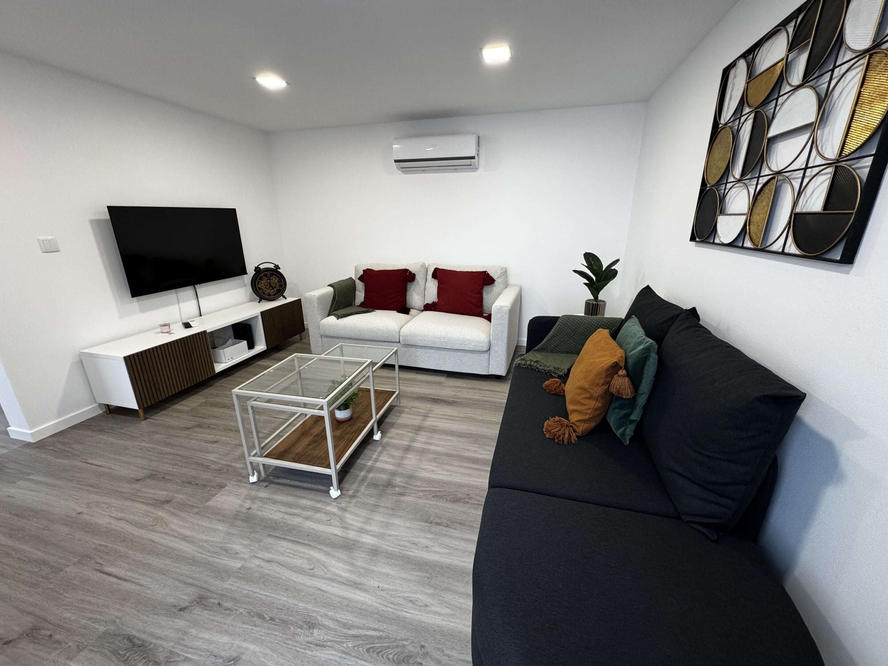 A modern living room with a flat-screen TV, a sofa, a coffee table, and a decorative wall piece.