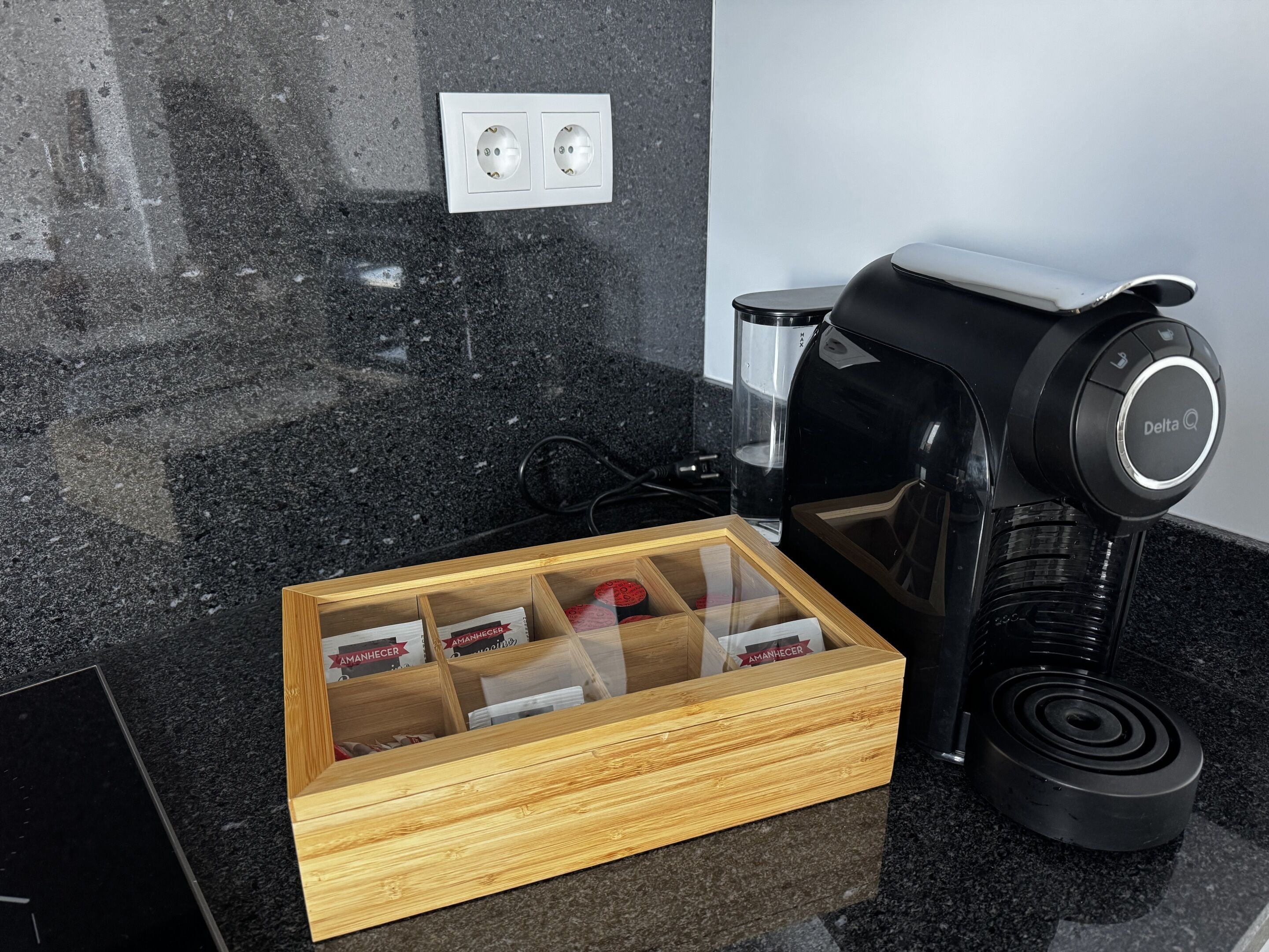 Eine Küche mit einer Kaffeemaschine, einer Schublade voller Kaffeekapseln und einer Steckdose an der Wand.