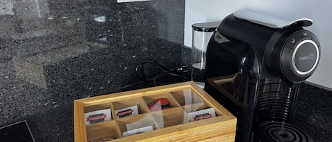 Eine Küche mit einer Kaffeemaschine, einer Schublade voller Kaffeekapseln und einer Steckdose an der Wand.