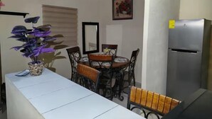 A compact kitchen with a dining table, chairs, a refrigerator, and a potted plant.