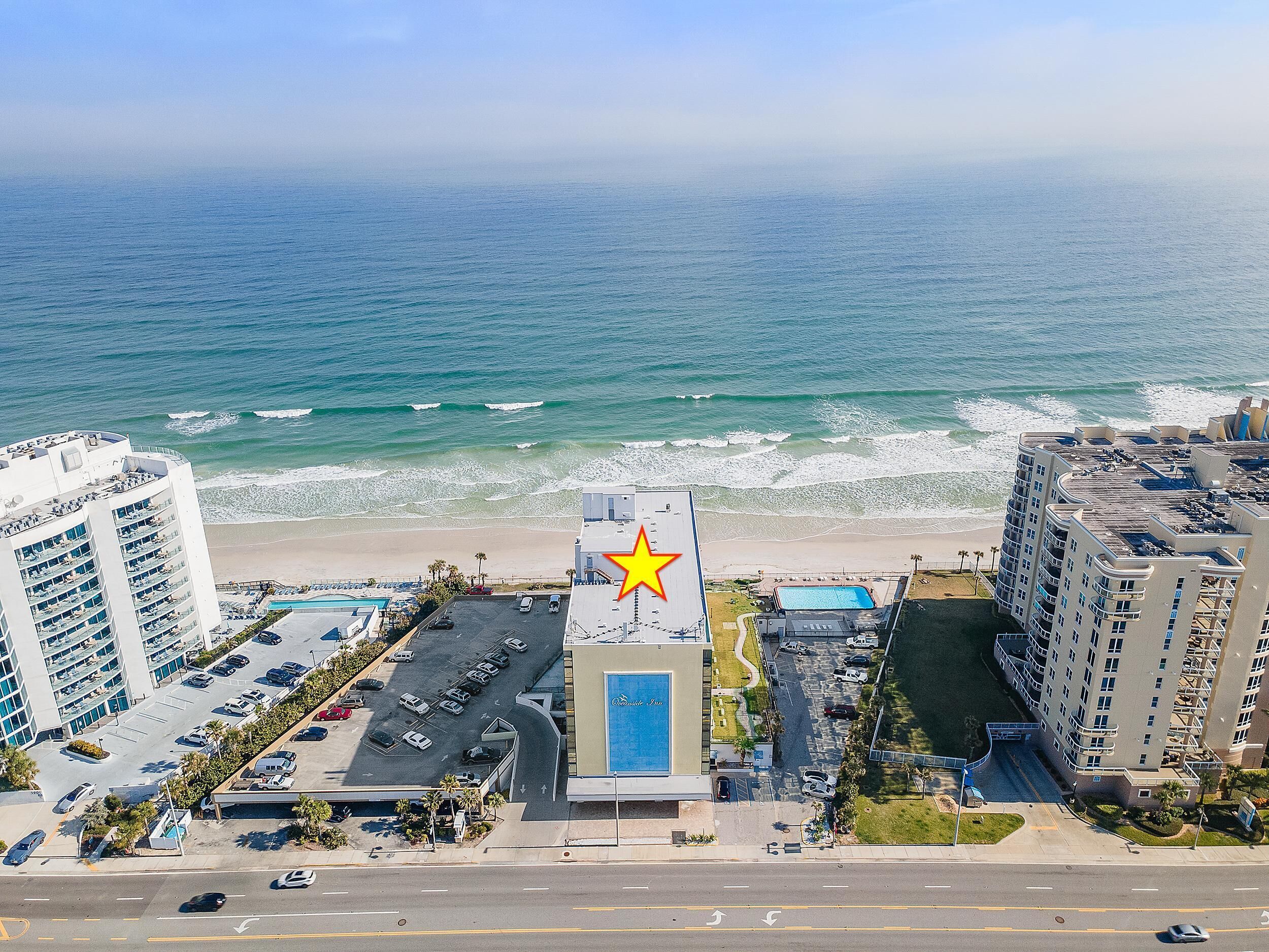 A hotel with a large swimming pool, a parking lot, and a view of the beach and ocean.
