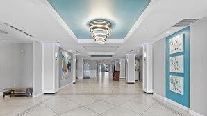 A modern hotel corridor with a tiled floor, a central light fixture, and artwork on the walls. - Oceanside Inn 313 (Daytona Beach Shores)