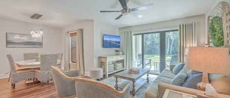 A modern living room with a dining area, a ceiling fan, and a large window with curtains.