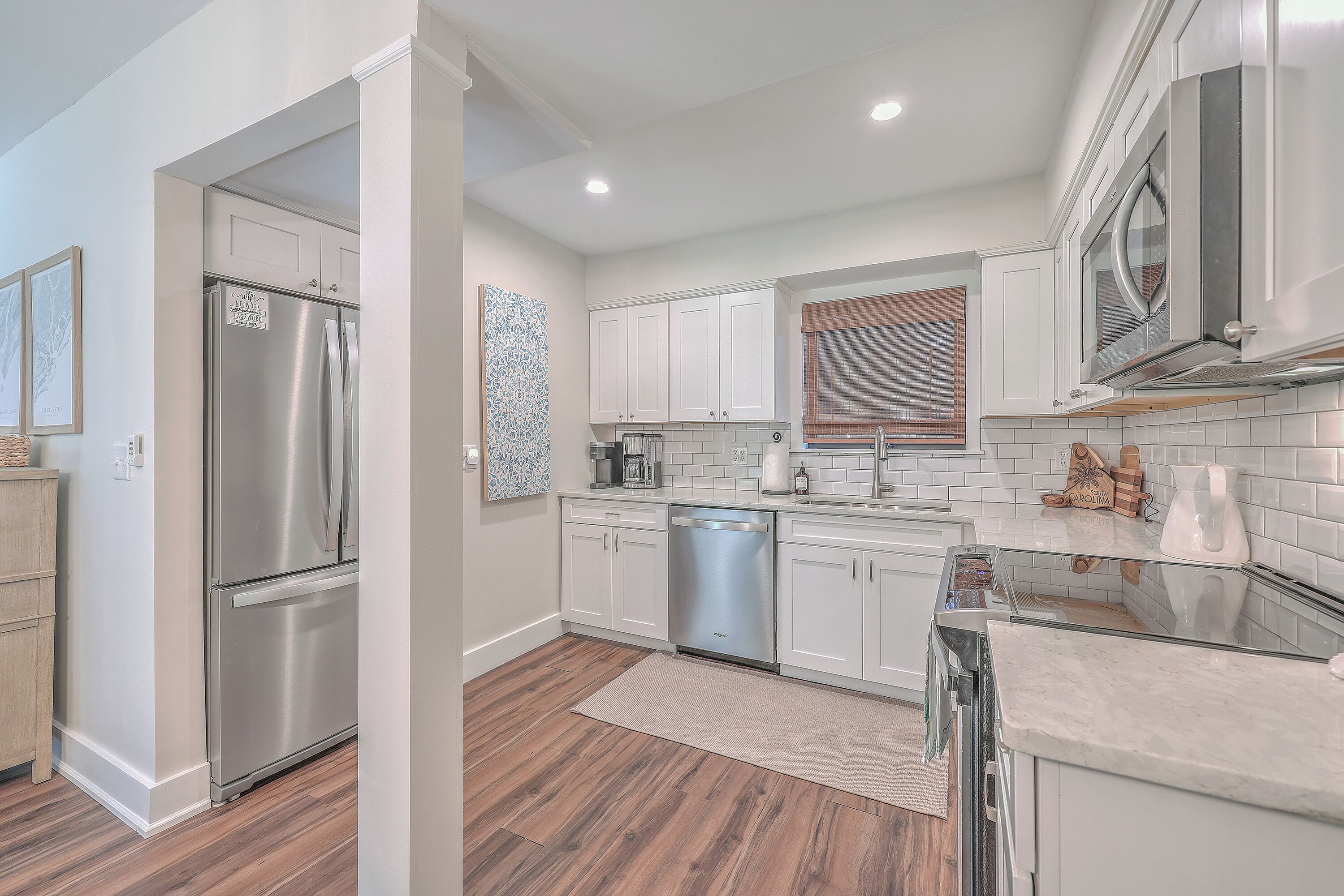 A modern kitchen with white cabinetry, stainless steel appliances, and a wooden floor.