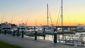 Un port de plaisance où de nombreux bateaux sont amarrés à des quais en bois, au moment du coucher du soleil.