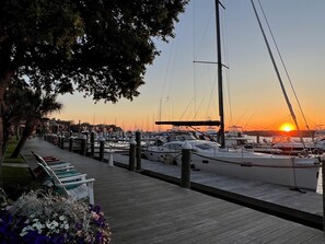 Ein Yachthafen mit vertäuten Booten, einer Holzpromenade und einem Sonnenuntergang im Hintergrund.