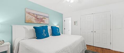 A bedroom with a bed, white nightstands, a ceiling fan, a painting, and white doors.