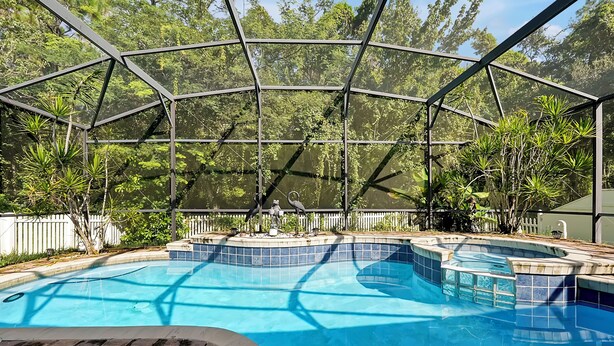 Una piscina con cerramiento de vidrio, rodeada de abundante vegetación y una cerca blanca.
