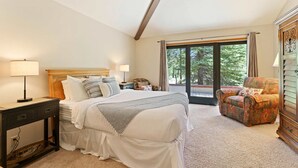 A bedroom with a bed, bedside tables, a chair, a dresser, and a large window with a view of trees. - 10 Tan Oak (Bend)