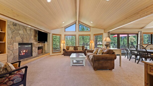 A spacious living room with a stone fireplace, large windows, and a high ceiling. - 10 Tan Oak (Bend)