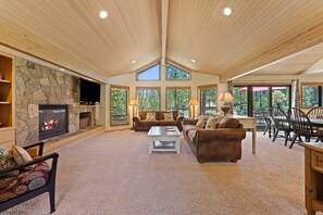 A spacious living room with a stone fireplace, large windows, and a high ceiling. - 10 Tan Oak (Bend)
