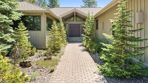 A building with a brick pathway leading to a double door entrance, surrounded by evergreen trees. - 10 Tan Oak (Bend)