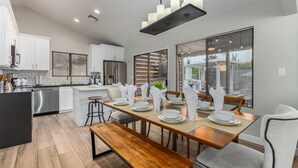 A modern kitchen with white cabinets, a stainless steel refrigerator, and a dining area with a wooden table and chairs. - 110th Scottsdale (Scottsdale)
