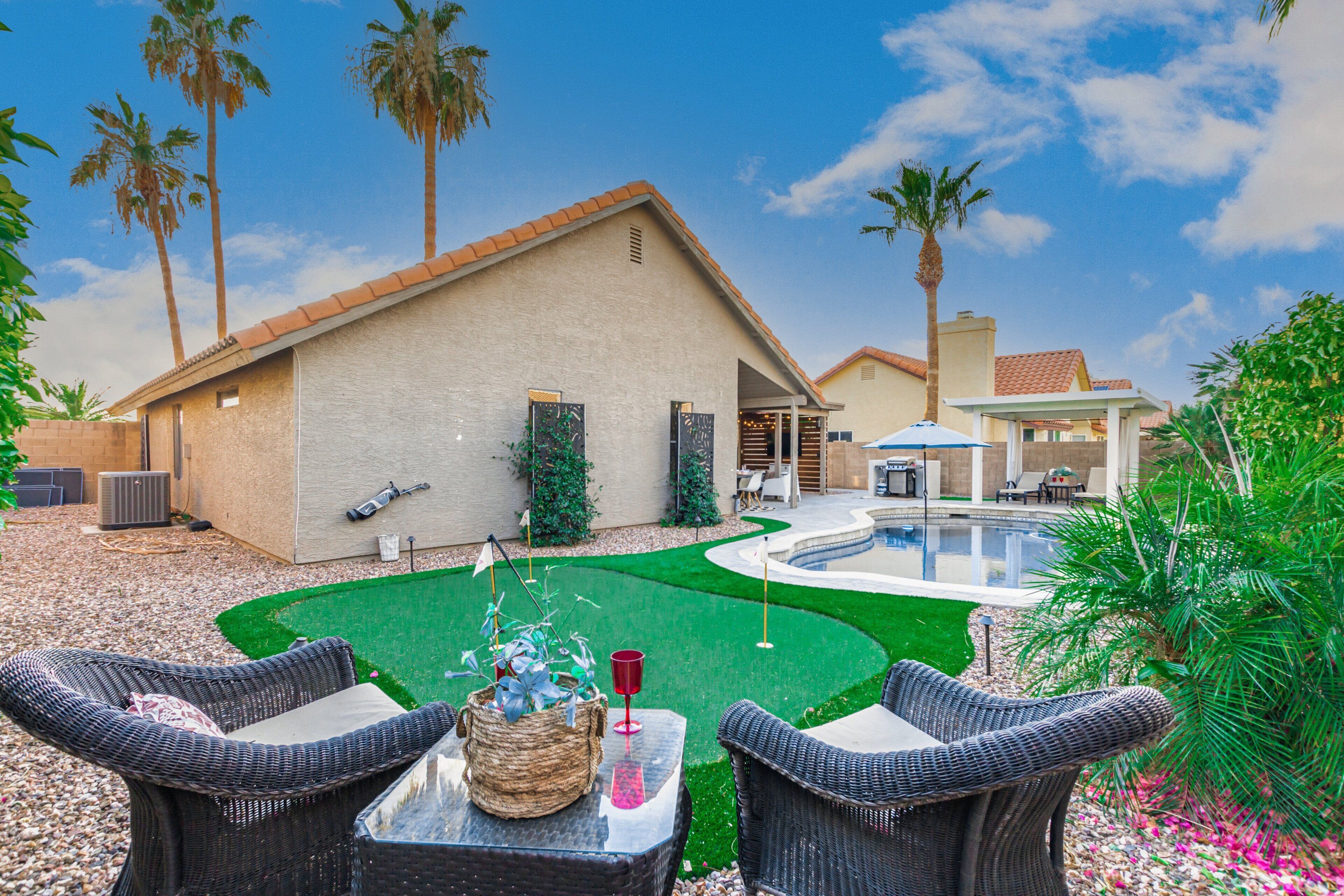 A backyard with a swimming pool, outdoor furniture, and palm trees.