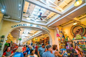 Een drukke overdekte markt met een boog waarop 'Charleston City Market' staat en verschillende winkels.