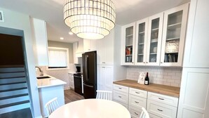 Una cocina moderna con armarios blancos, una isla central, una mesa de comedor con sillas y una botella de vino en la encimera.