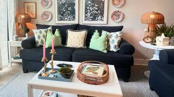 A living room with a black sofa, patterned cushions, a white coffee table, and wall decor.