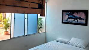 Quarto com cama, janela, ventoinha no teto e um quadro na parede.