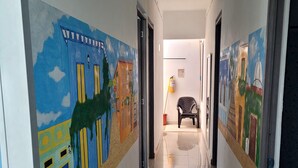 Um corredor com murais coloridos nas paredes, uma cadeira ao centro e uma porta no final.