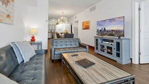 Una sala de estar moderna con un sofá de cuero, una mesa de centro de madera y un mueble de televisión con una pintura de un paisaje urbano.