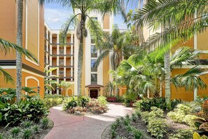 A courtyard with a central pathway, surrounded by palm trees and various plants, leading to a building with multiple balconies. - 12538 International Drive #c303 Orlando, 2bed (Orlando)