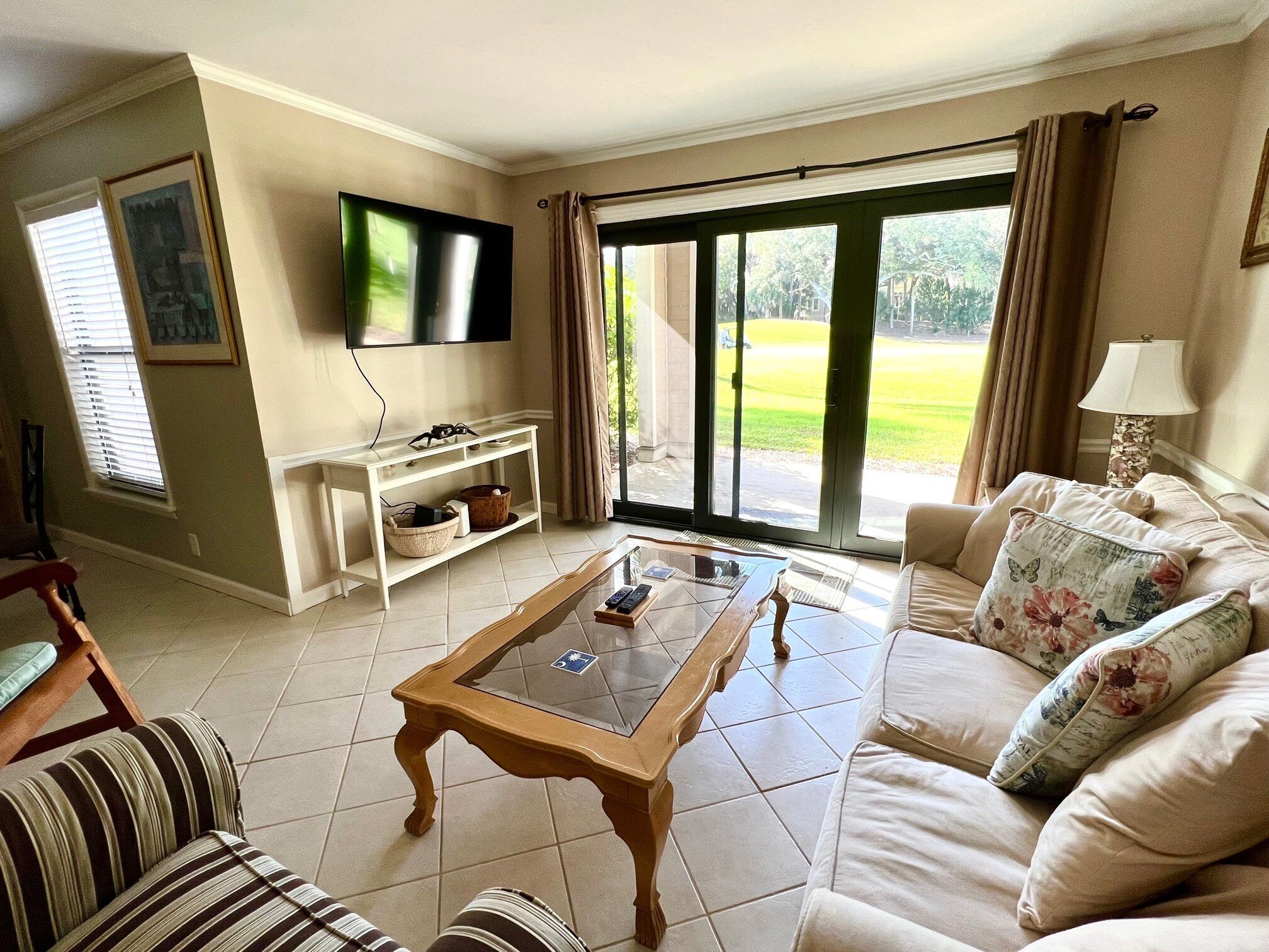 Un salon comprenant un canapé, une table basse, un téléviseur et une porte-fenêtre coulissante donnant sur un jardin.