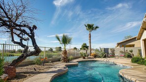 A swimming pool with a curved edge, surrounded by a fence, palm trees, and a variety of plants. - 120th Avondale (Avondale)