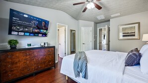 A hotel room with a bed, a dresser, a TV mounted on the wall, and a ceiling fan.