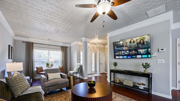 A living room with a ceiling fan, a TV mounted on the wall, a round coffee table, and a sofa.