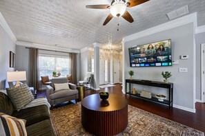 Ein Wohnzimmer mit Deckenventilator, Wand-Fernseher, rundem Couchtisch und einer Couch.